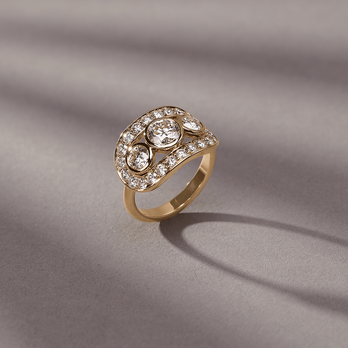 Heritage Trio Ring i 18 karat gull fotografert i vinkel på en strukturert grå bakgrunn med myke skygger.