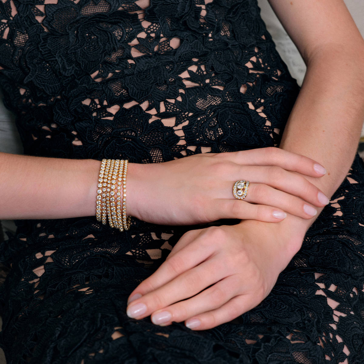 Lumi Bracelet vist lagvis på håndleddet sammen med en ring, nærbilde av hånd i blondekjole