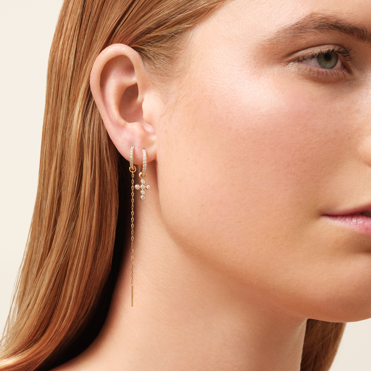 Modell iført Diamond Cross Ear Pendant fra Julie Sandlau kombinert med en diamantbesatt hoop og en kjedeøredobb