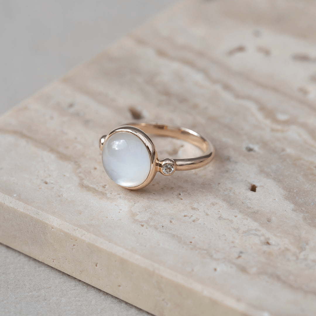 Carla Ring i gull med hvit cabochon-slipt stein, foto på steinsokkel