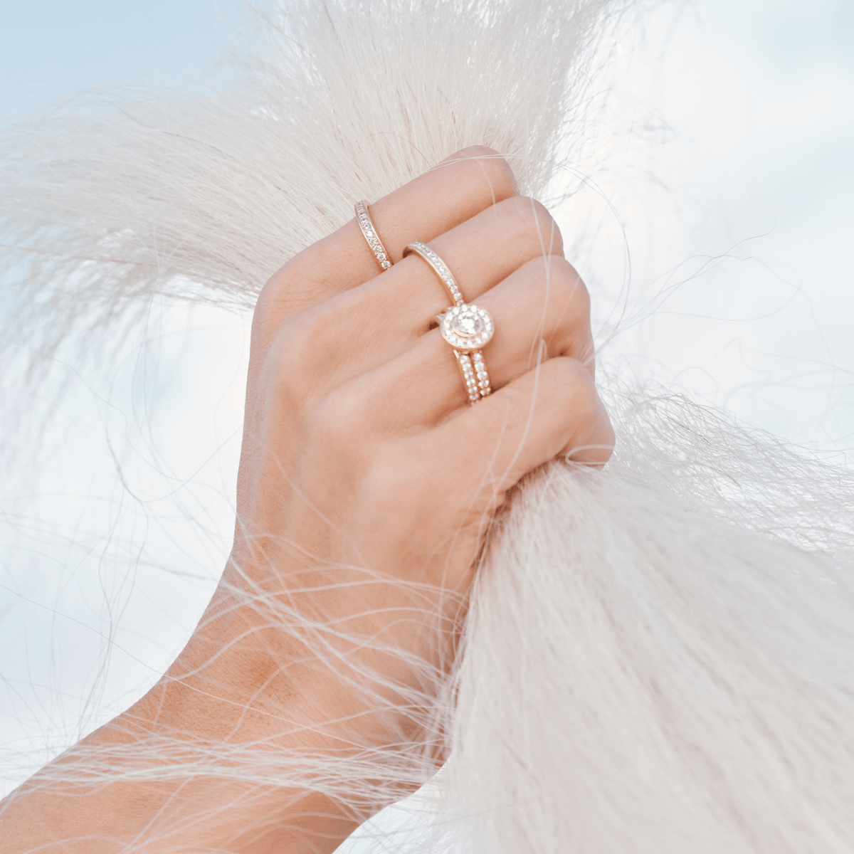 Modell bærer en stack av gullringer med diamanter, blant annet Heritage P.S. Ring, mens hånden holder fast i hvit pels