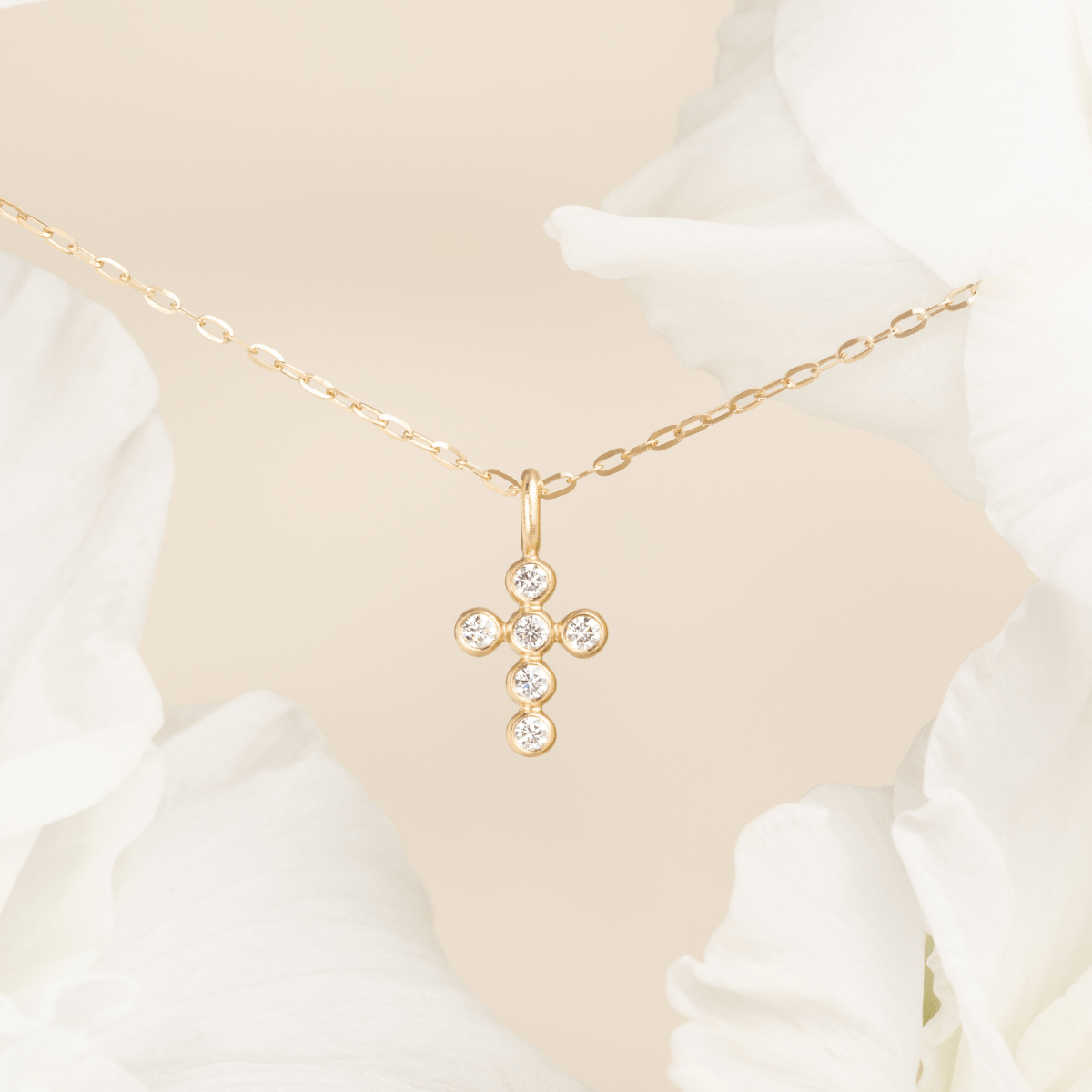Diamond Cross Pendant på gullkjede mellom hvite blomsterblader