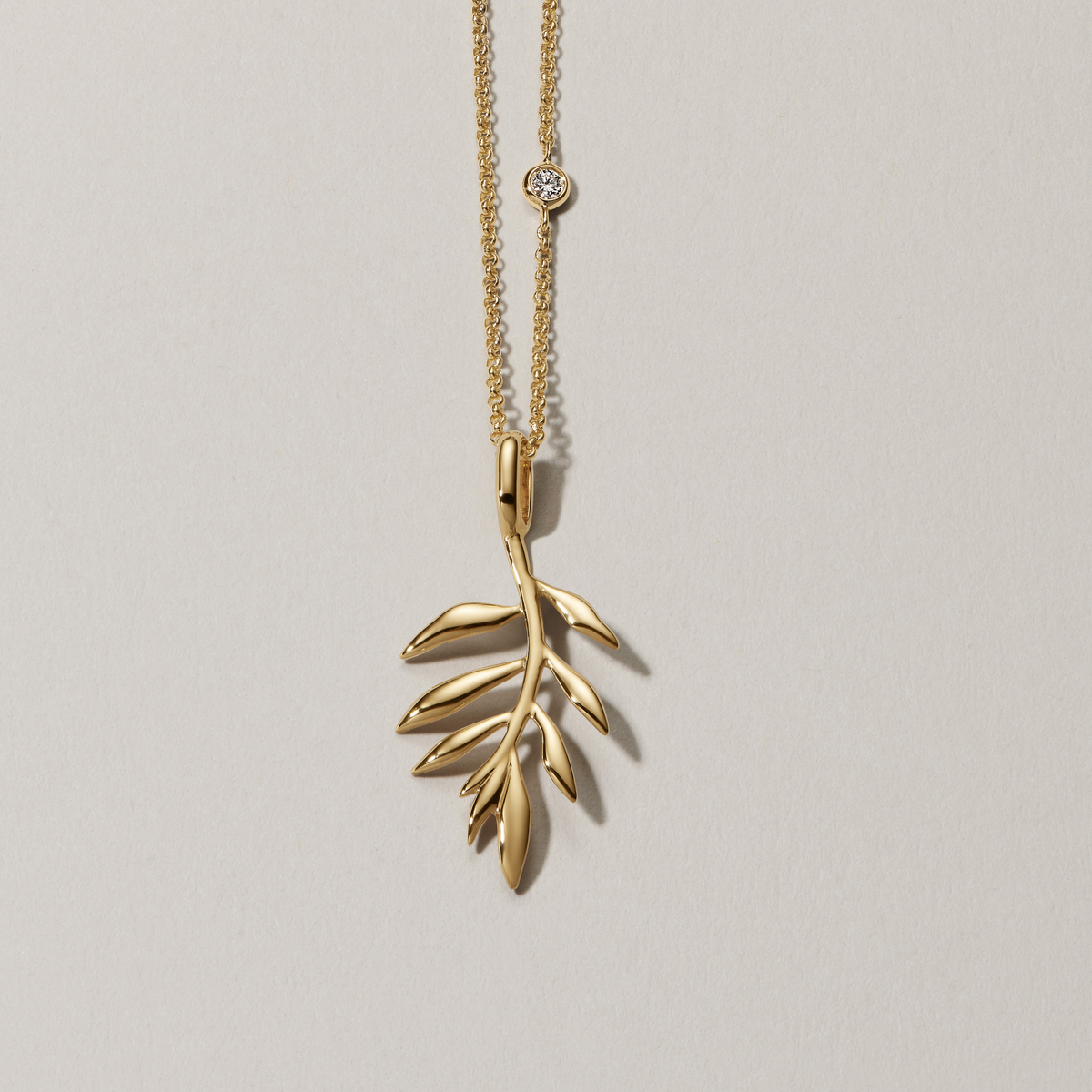 Tree of Life Pendant i 18K gull på gullkjede med liten diamant, hengende foran lys bakgrunn