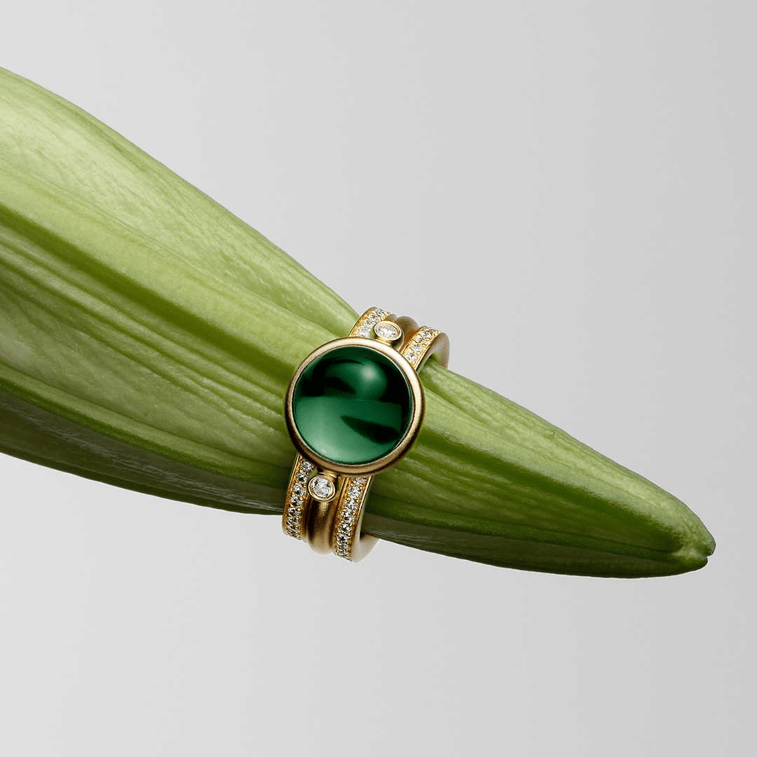 Billedfeil: Nærbilde av samme gullring med grønn cabochon-sten og diamanter mot et blad, stemmer ikke med Prime Double Infinity Look (tre separate ringer).