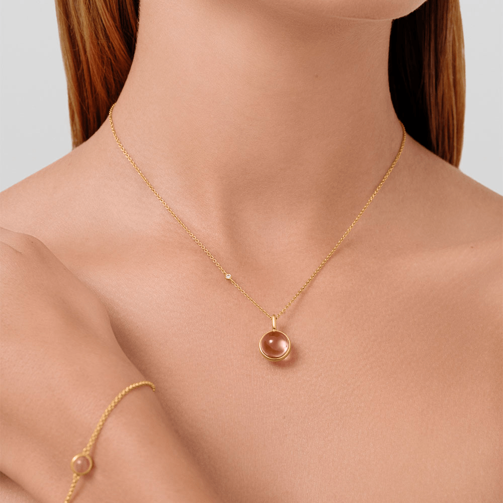 Julie Sandlau anheng med lyserosa cabochon-krystall båret om halsen, med et matchende armbånd skimtet på håndleddet