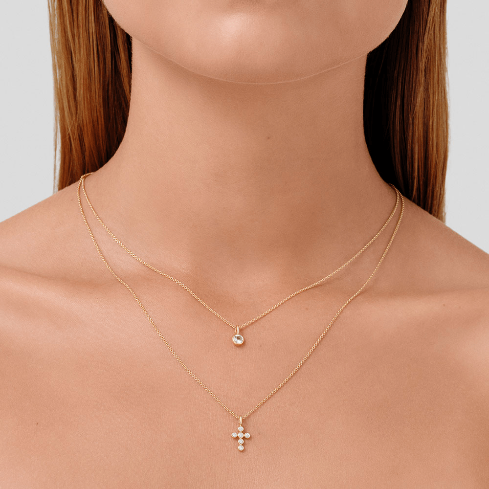 Modell bærer Diamond Cross Pendant lagvis med et lite solitær-anheng på gullkjeder