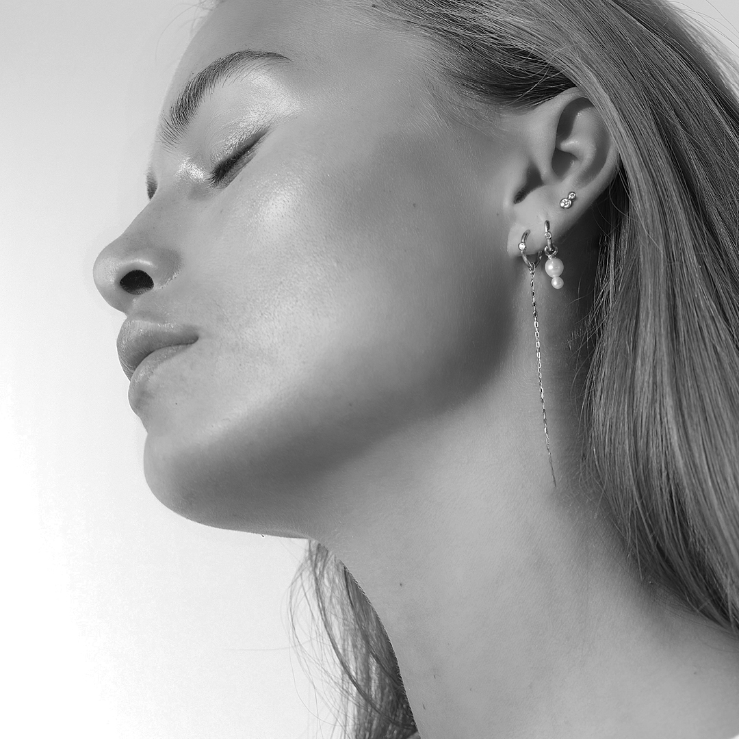 Svart-hvitt bilde av modell med flere øreringer i øret, blant annet perlebesatt creol og diamantstikk fra Purity Medium and Eden Look