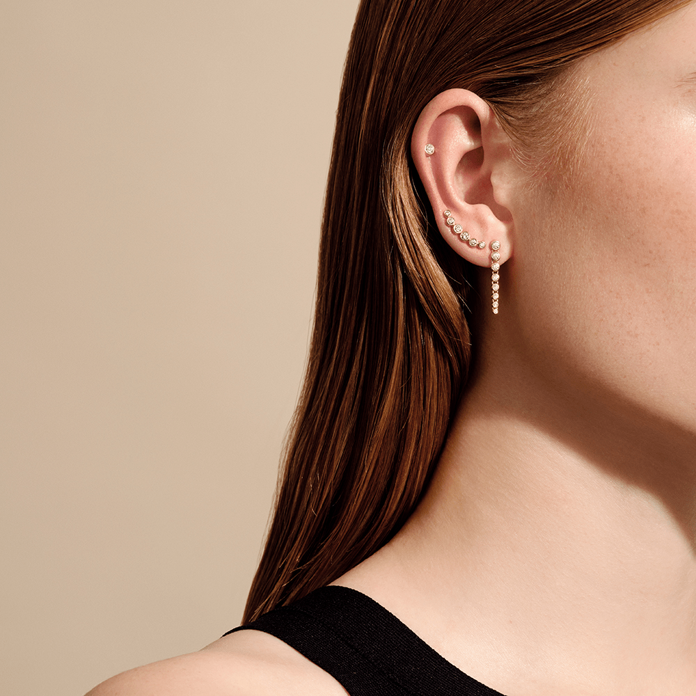 Luster Earstuds båret i øret sammen med ear cuff og hengende øredobb, modellbilde i sort topp.