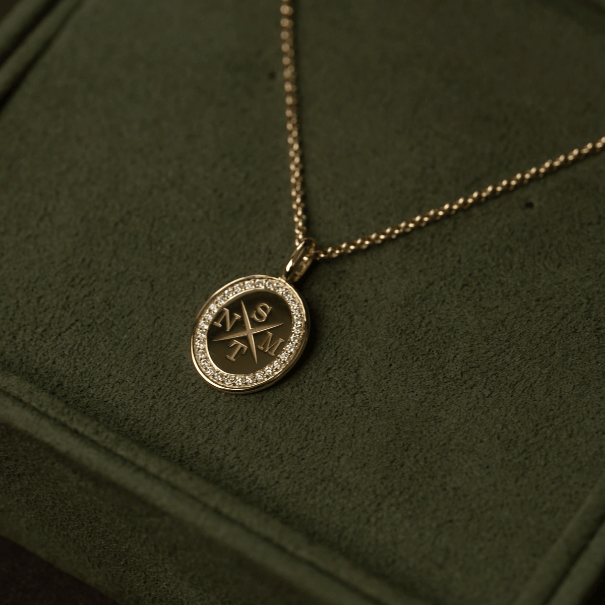Medallion halskjede i 18K gull med diamantkant og inngraveringen NSTM, nærbilde