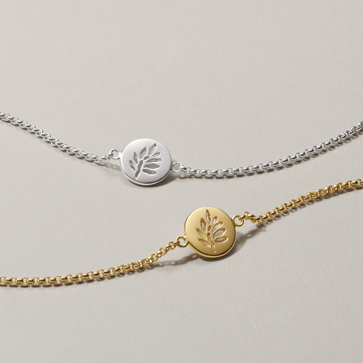 Signature Bracelet sammenlignet med en tilsvarende modell i gull, begge med kjedearmbånd og bladmedaljong.