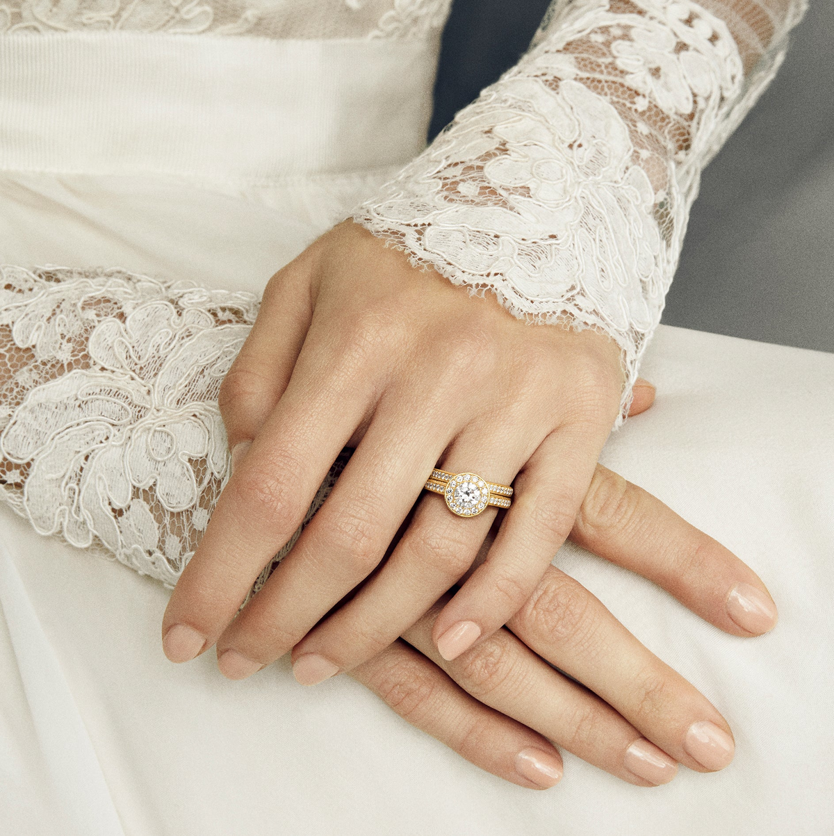Modell i brudekjole med blondeerme bærer Medium Eternity Diamond Band stablet med en halo-forlovelsesring